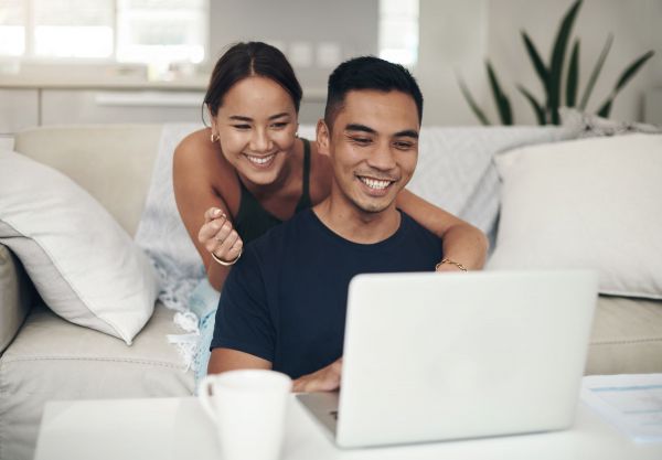 A couple smiling and looking at a laptop together on a sofa, with a cup in the foreground.