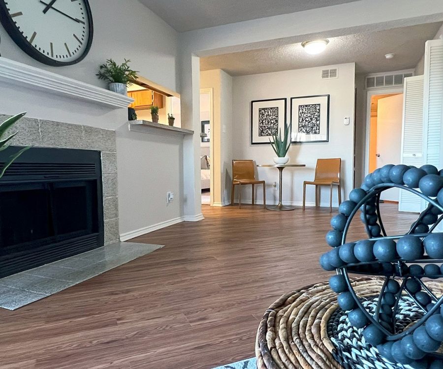 Modern living room with fireplace, clock, and decorative objects. Dining table with chairs in the background.