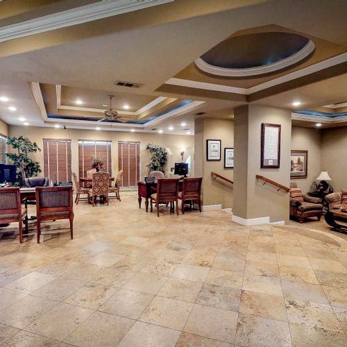 Spacious clubhouse area with beige tile floor, wooden furniture, recessed lighting, and a TV mounted on the wall.