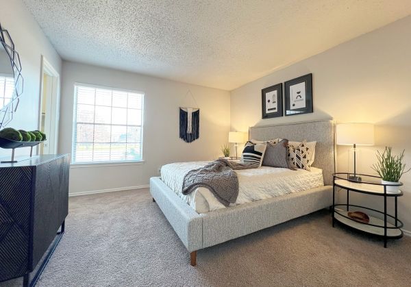 Cozy bedroom with a large bed, decorative pillows, two lamps, wall art, and a window letting in natural light.